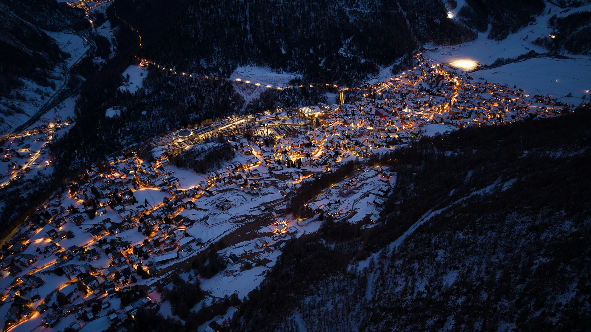 Illuminated snow-covered ski resort, seen from the air at night